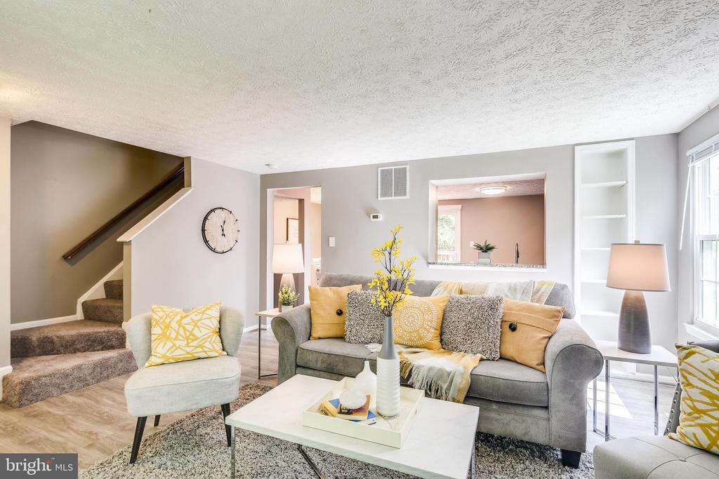 Staged living room with a gray sofa, yellow accents, white coffee table, and staircase.