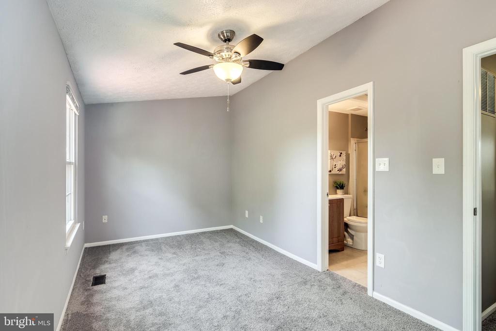 Vacant bedroom with gray carpet, ceiling fan, and doorway to an attached bathroom.
