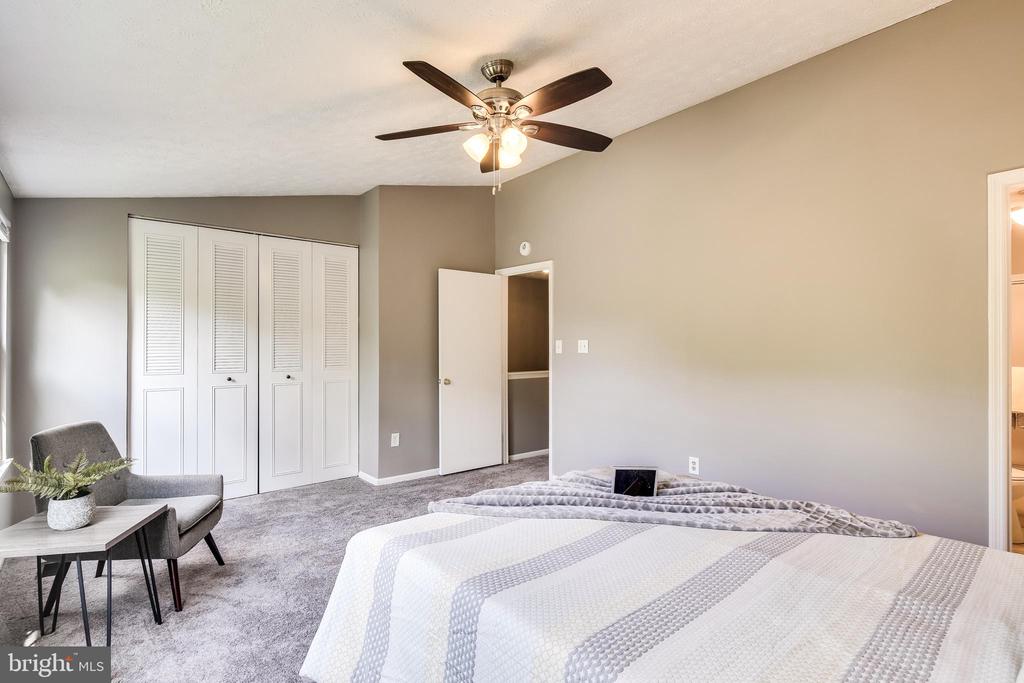 Bedroom with a bed, ceiling fan, louvered closet doors, and a small seating area.