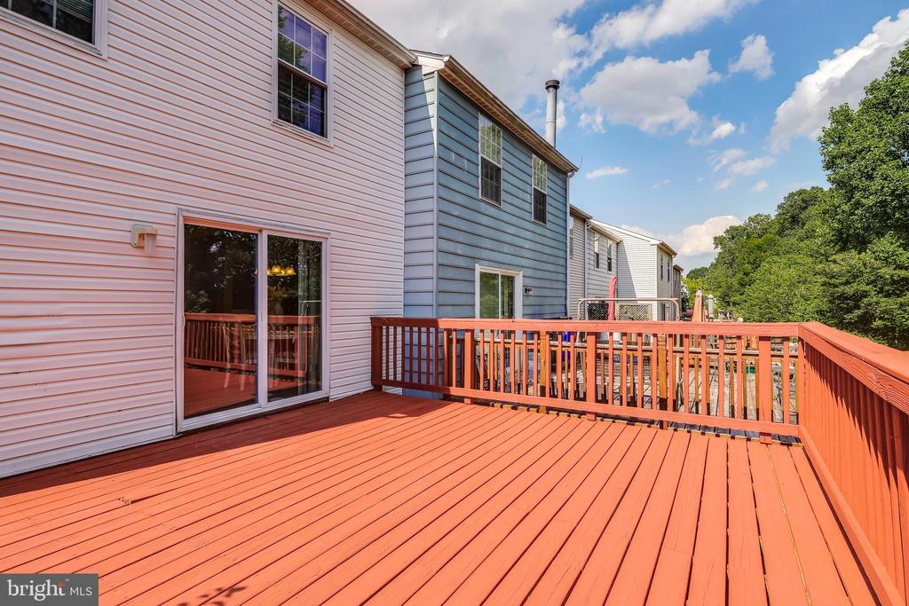 Spacious red wooden deck behind a home, with railings and a sliding glass door.