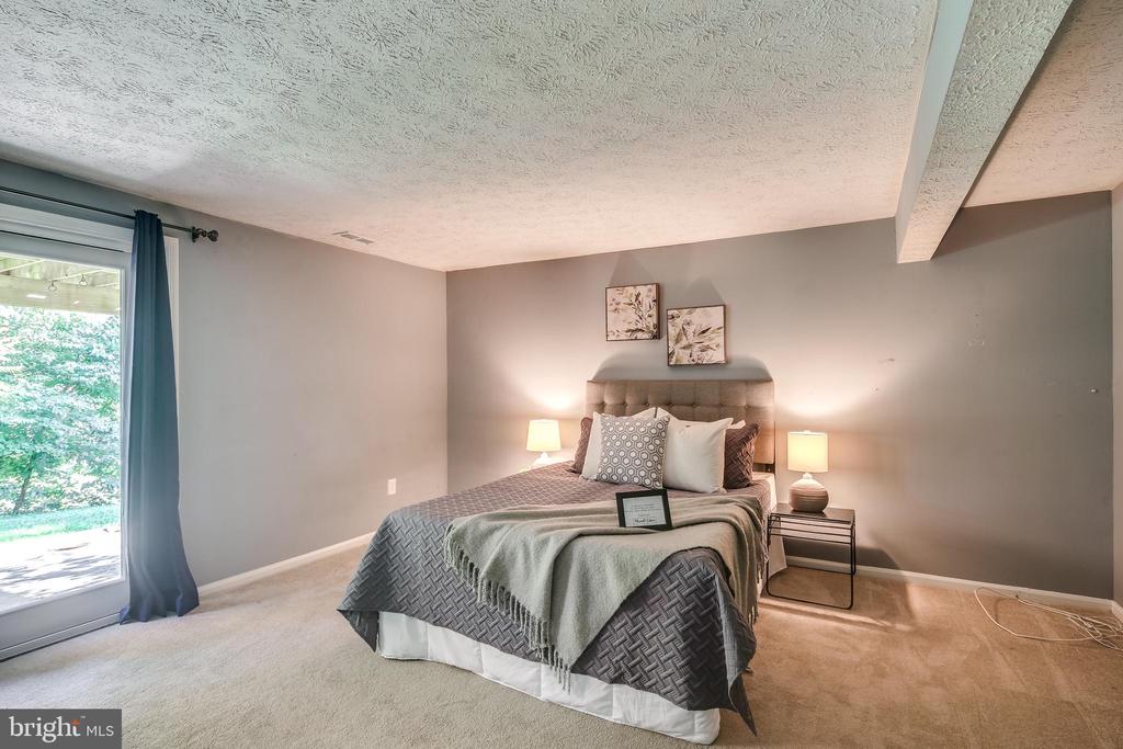 Staged bedroom with a gray upholstered bed and sliding glass door overlooking greenery.
