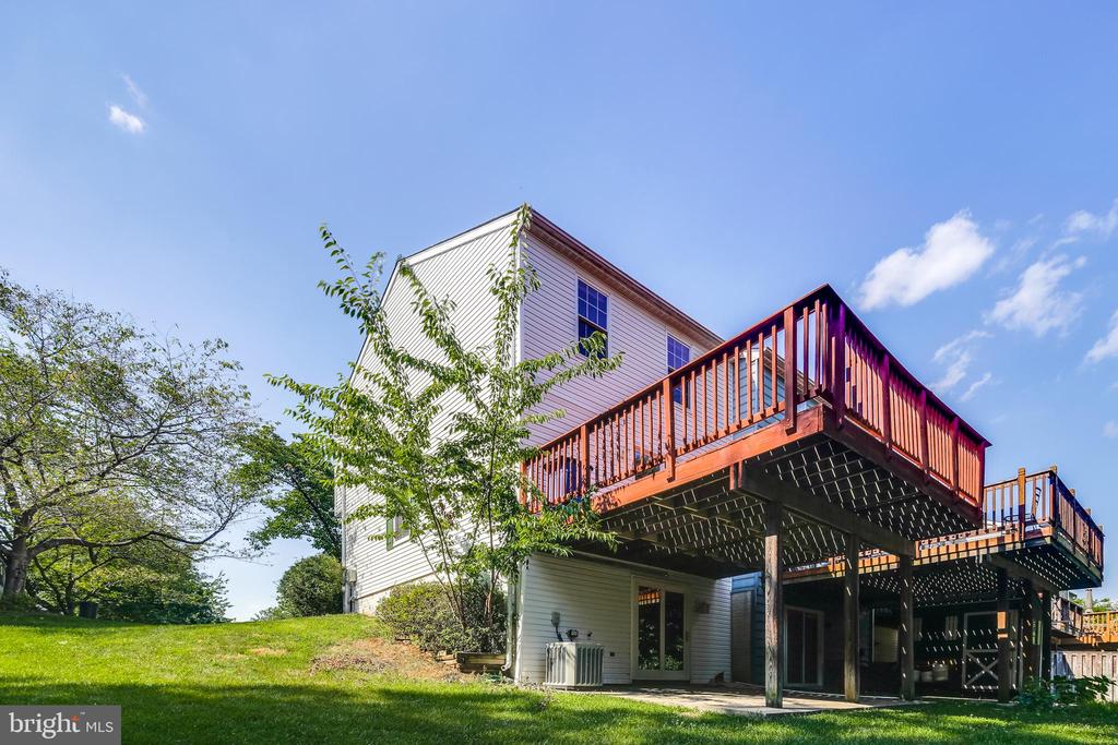 Rear of a two-story home with a large elevated wooden deck overlooking a green lawn.
