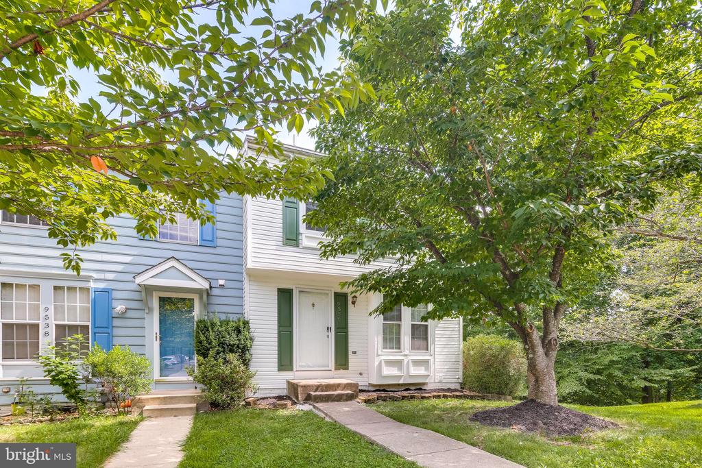 Attached home with light siding, blue front door, contrasting shutters, and a large shade tree.