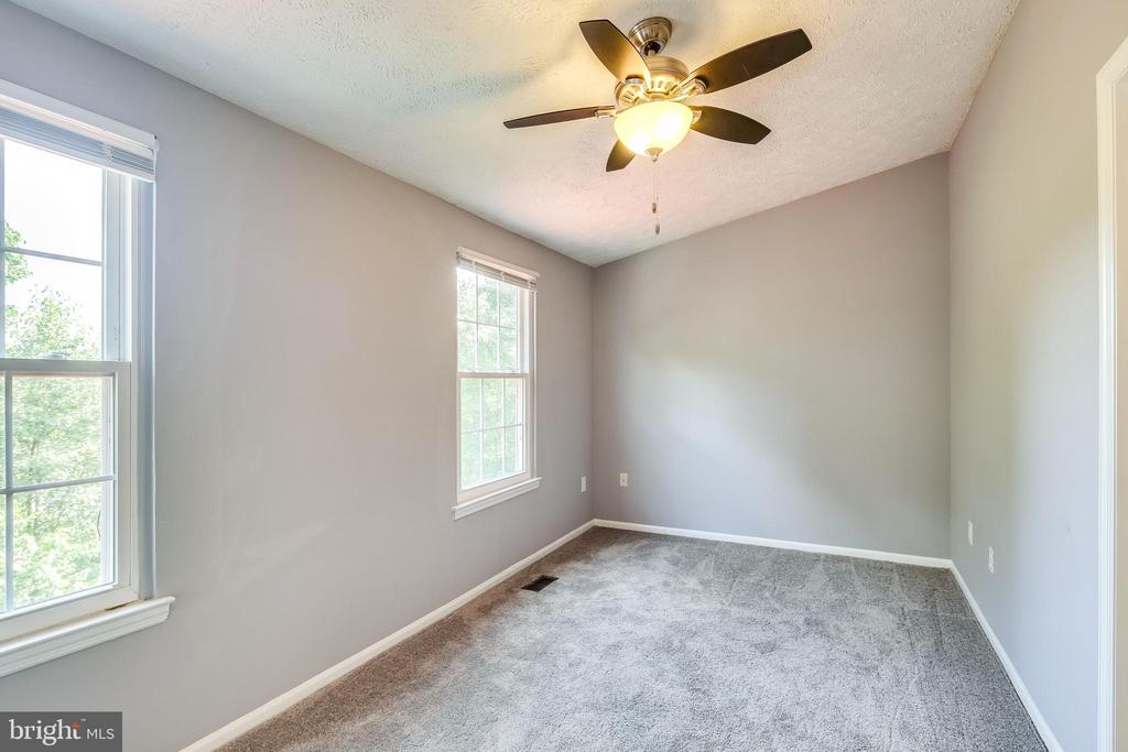 Empty bedroom with gray carpet, two windows, and a ceiling fan with light.