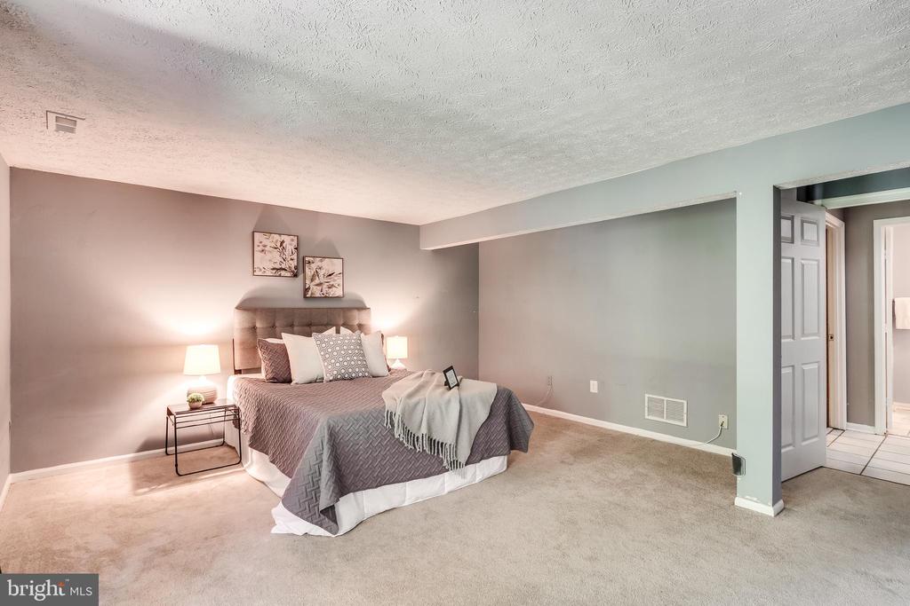 Staged bedroom with a gray upholstered bed, bedside lamps, and beige carpeting.