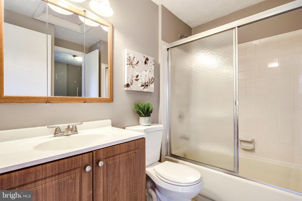 Bathroom with a wood vanity, mirrored cabinet, and bathtub behind a frosted-glass sliding door.
