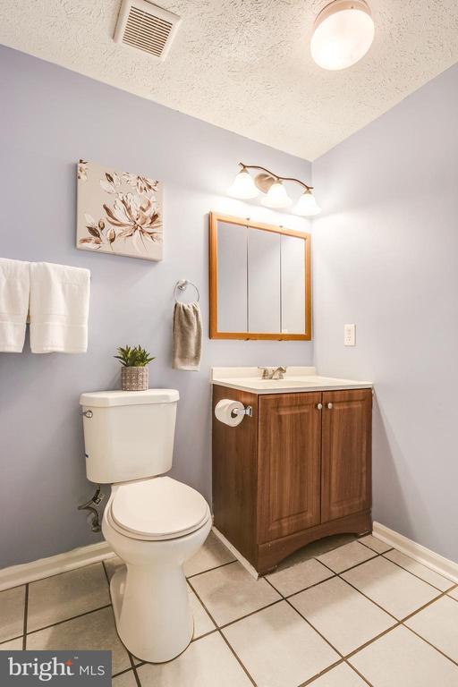 Bathroom with a wood-finish vanity, mirrored cabinet, and white toilet.