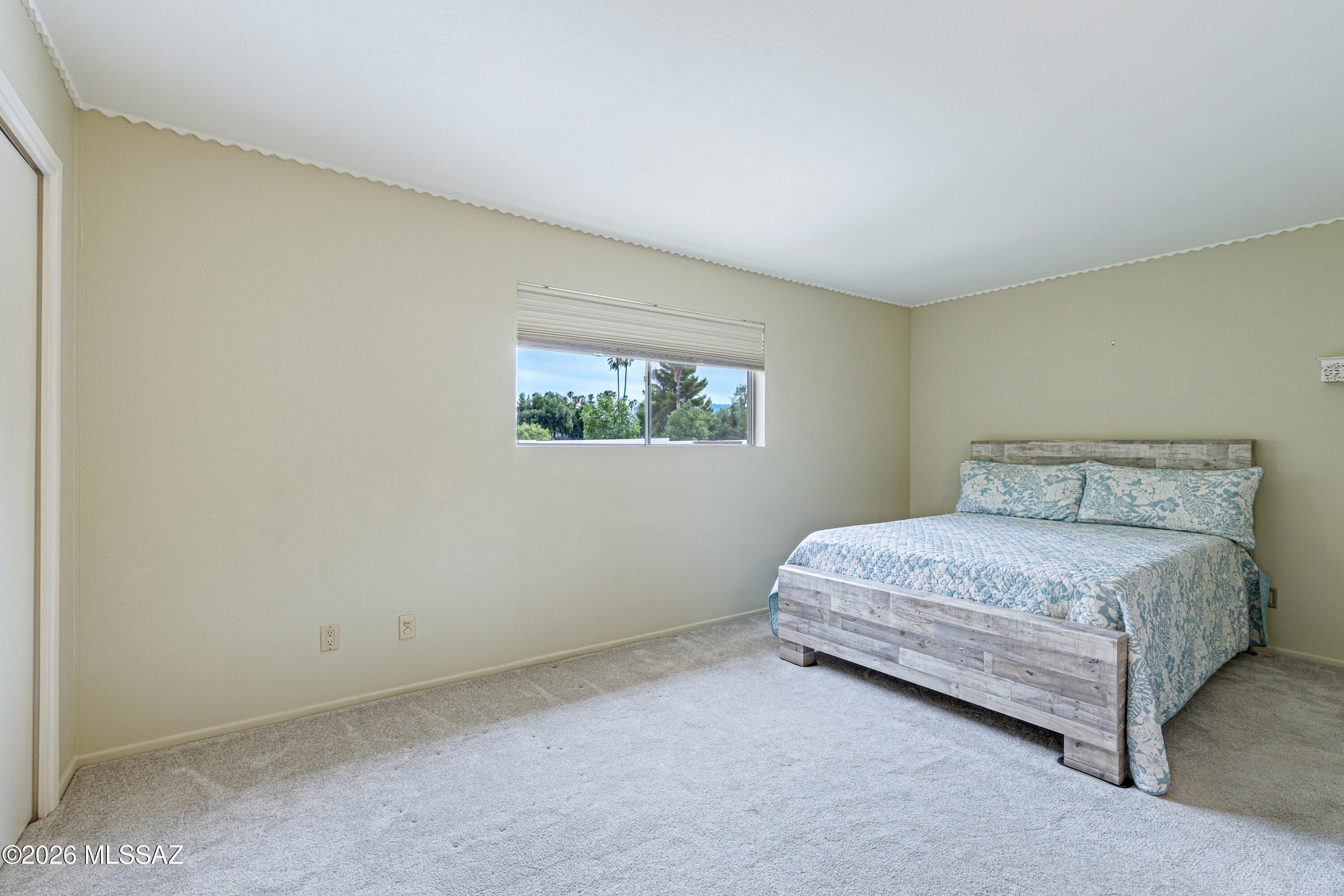 Bedroom with blue floral bedding, a gray wood bed frame, and a window overlooking trees.