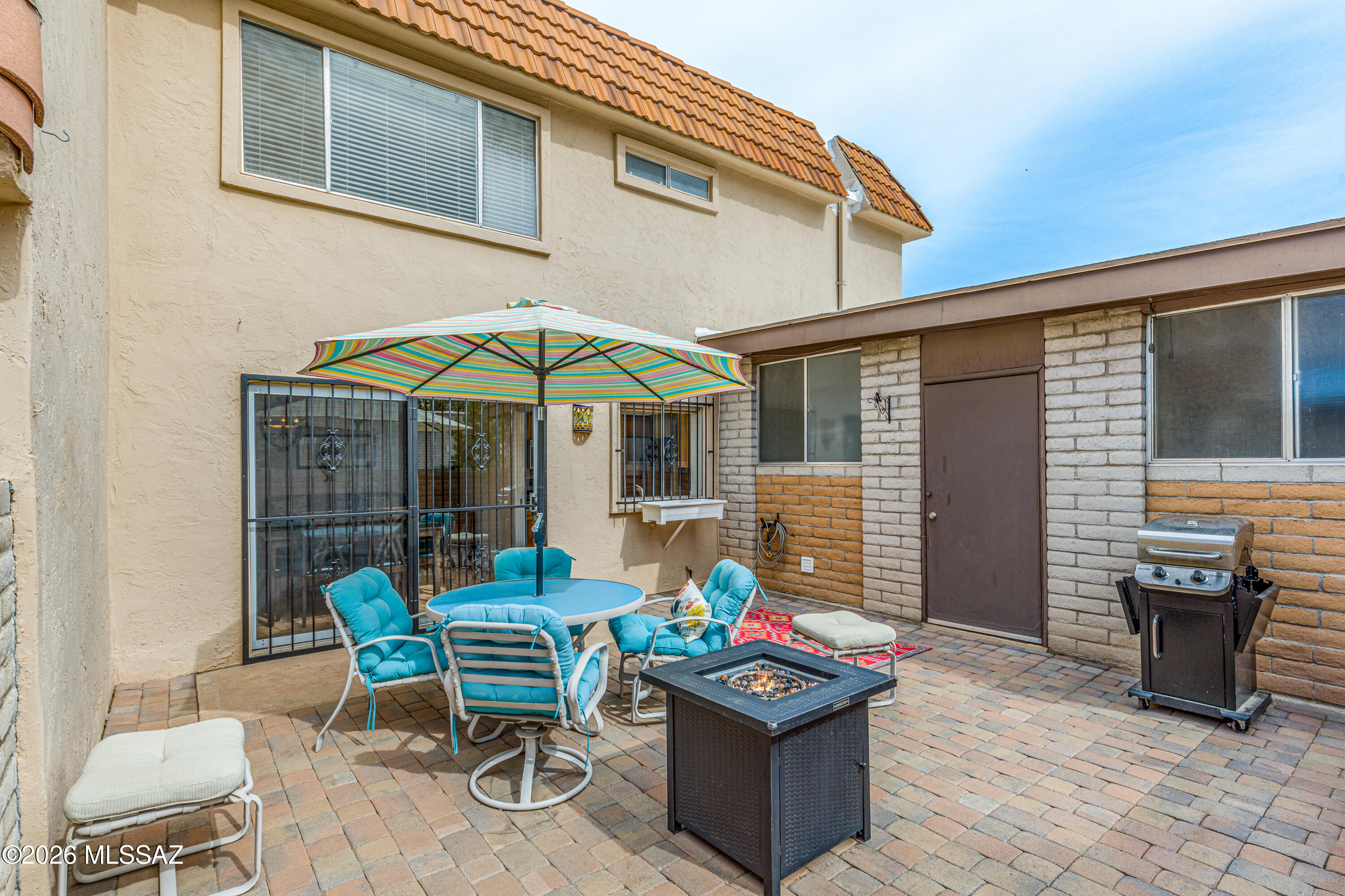 Backyard patio with turquoise seating under a striped umbrella, fire pit, and grill.