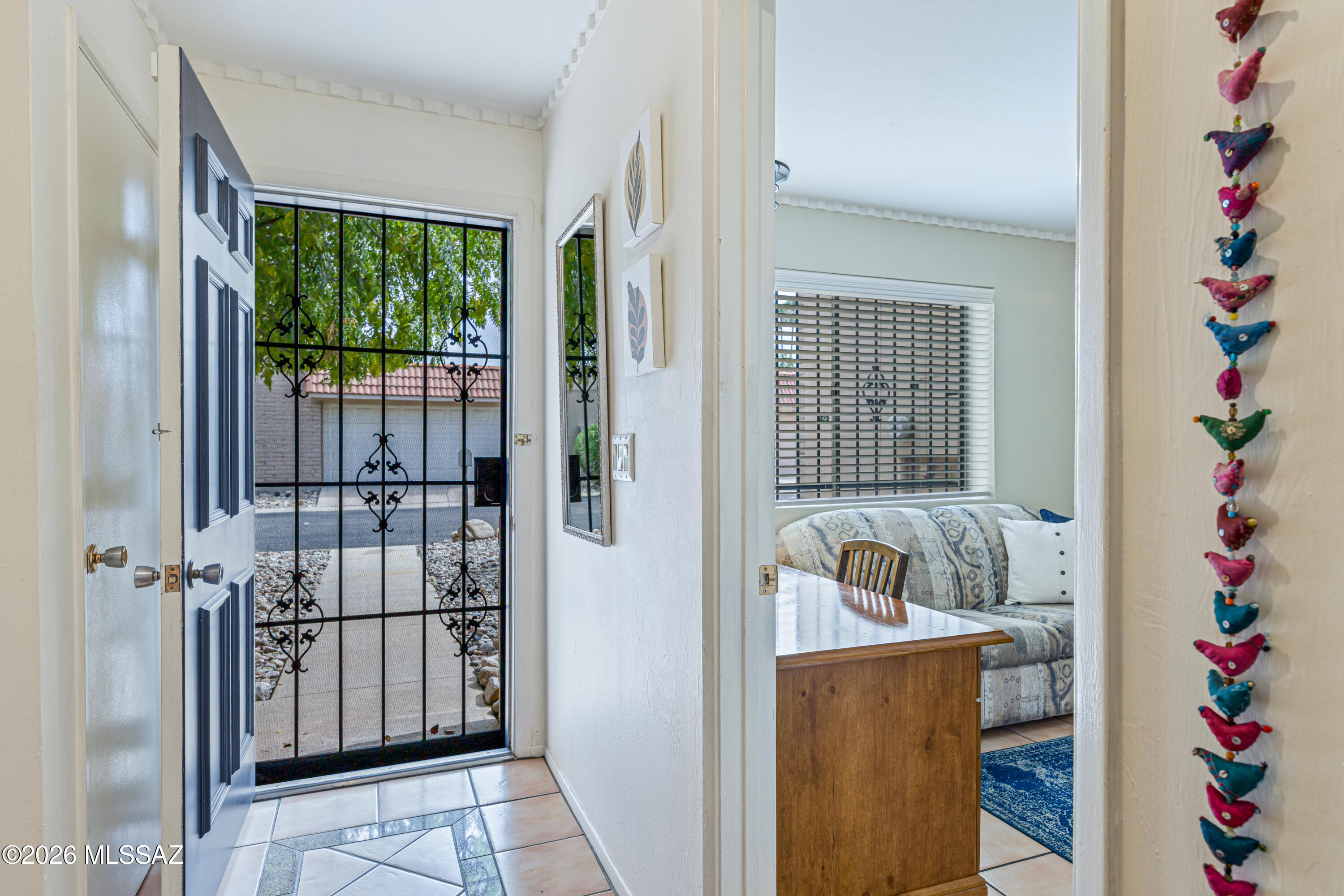 Entryway with an open front door and iron security gate, looking into a living area with a patterned sofa.