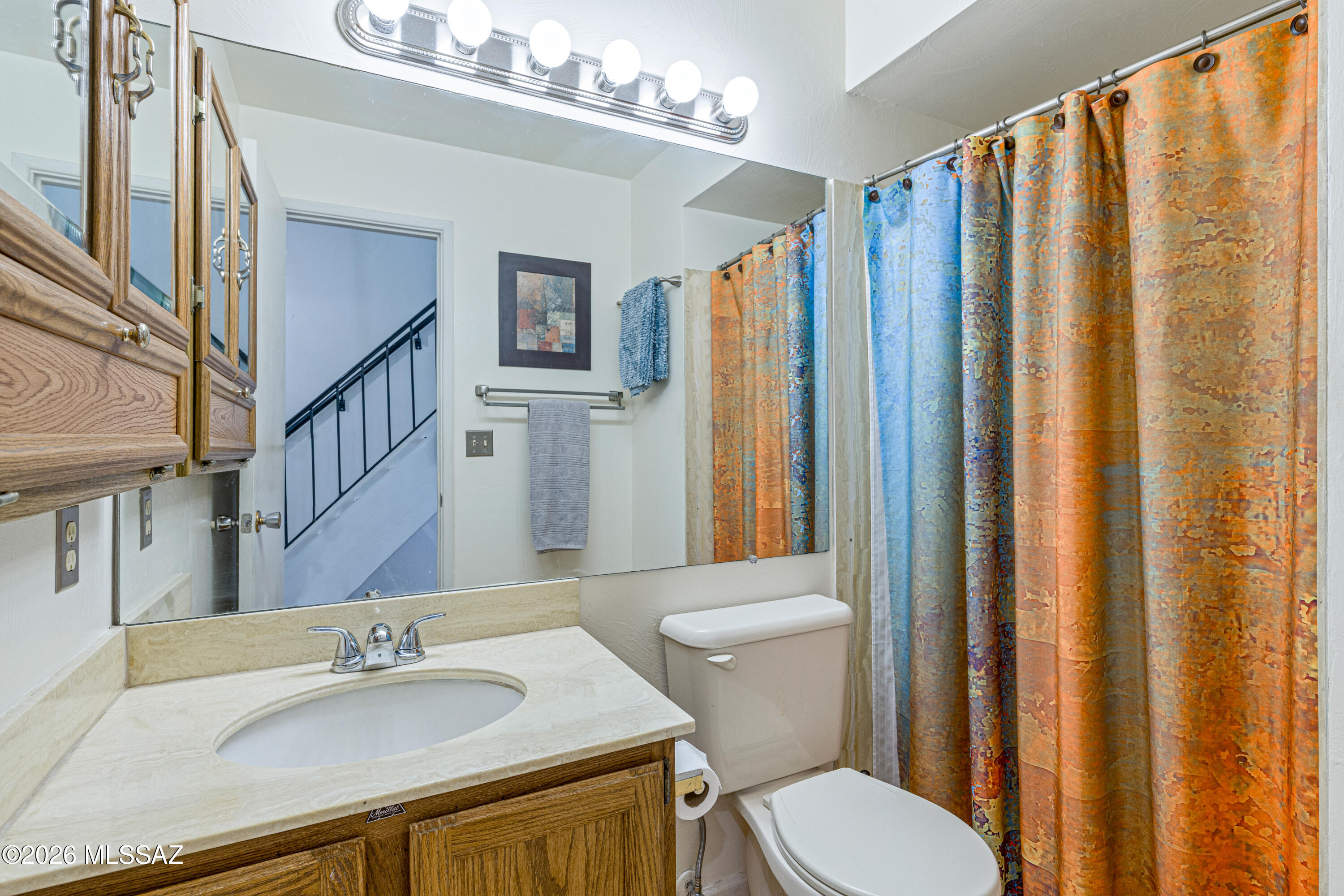 Bathroom with wood vanity, large mirror, and colorful patterned shower curtain.