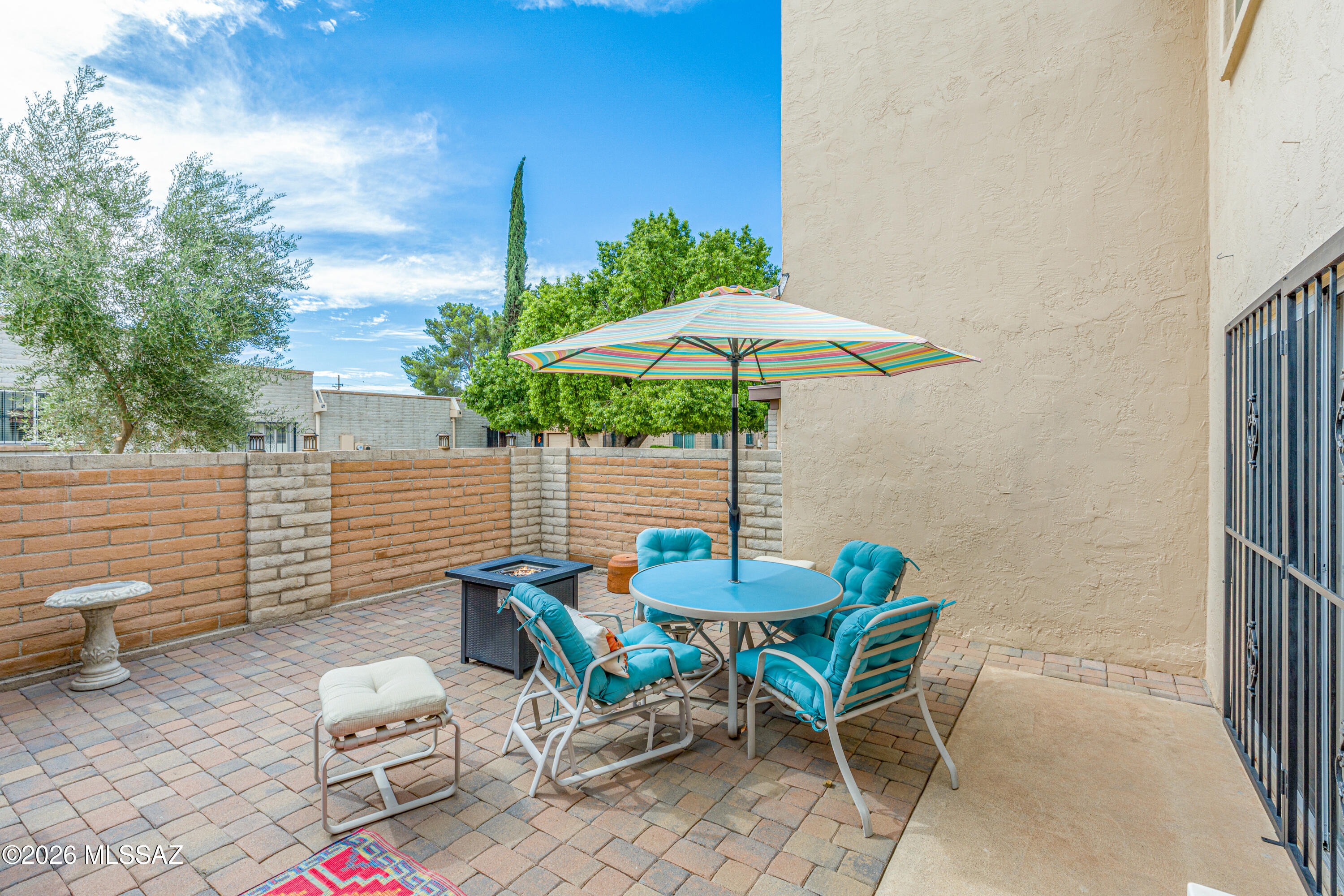 Furnished brick patio with turquoise seating and a striped umbrella beside the house.