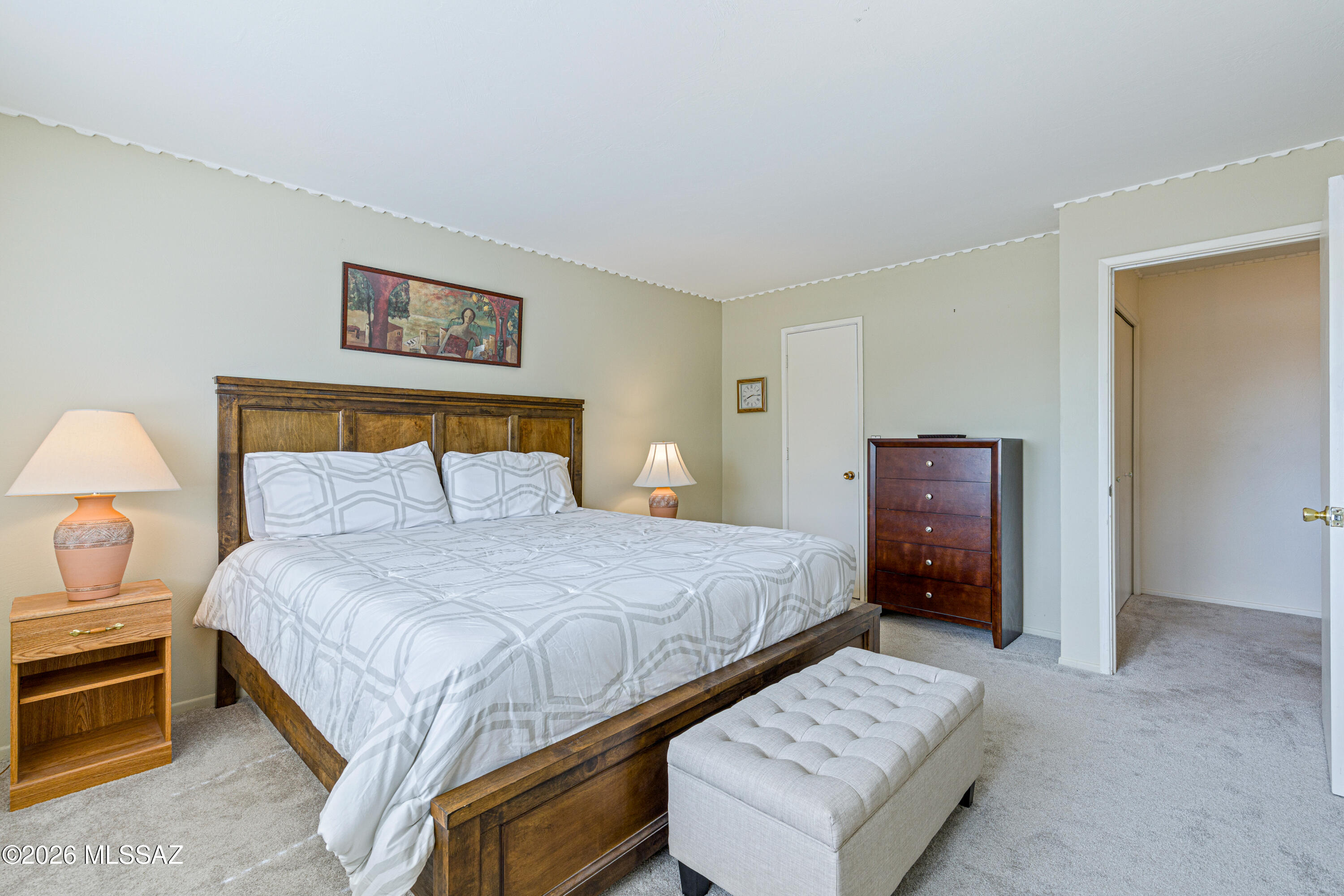 Furnished bedroom with a wooden bed, geometric bedding, and a tufted bench at its foot.