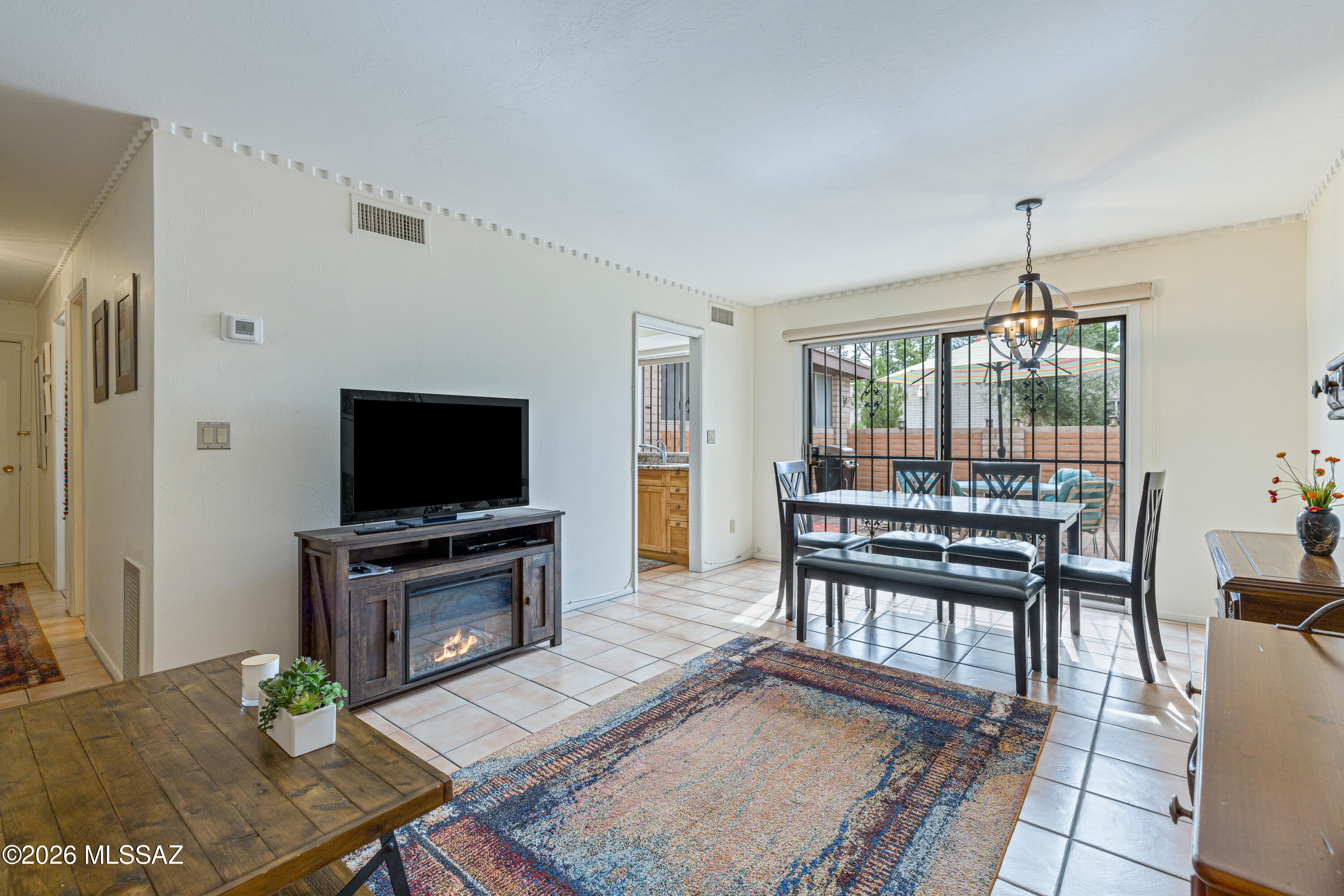 Living and dining room with a fireplace console, colorful rug, and sliding glass doors to a brick patio.