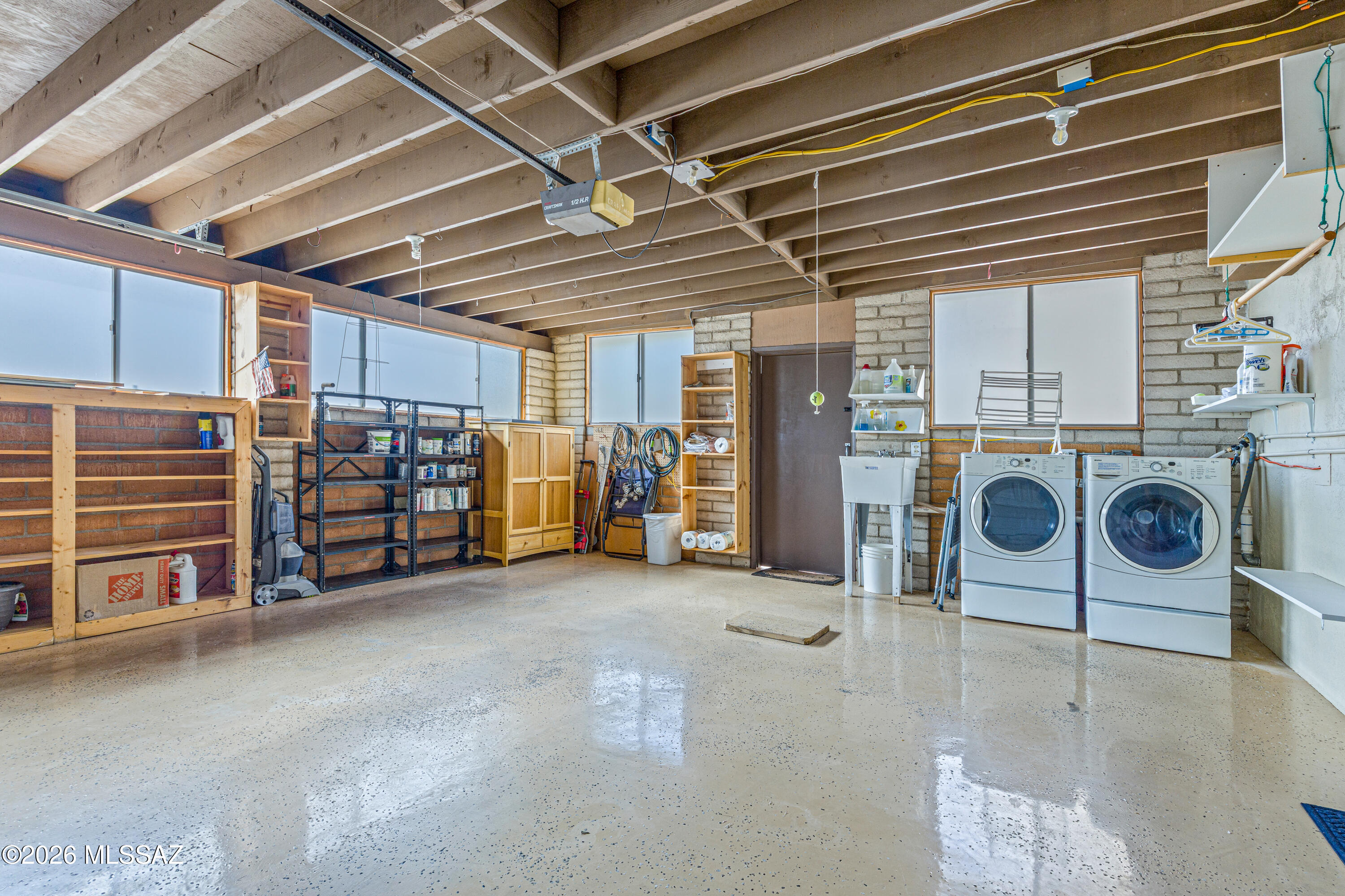 Garage with exposed ceiling beams, organized storage shelves, and a washer and dryer.