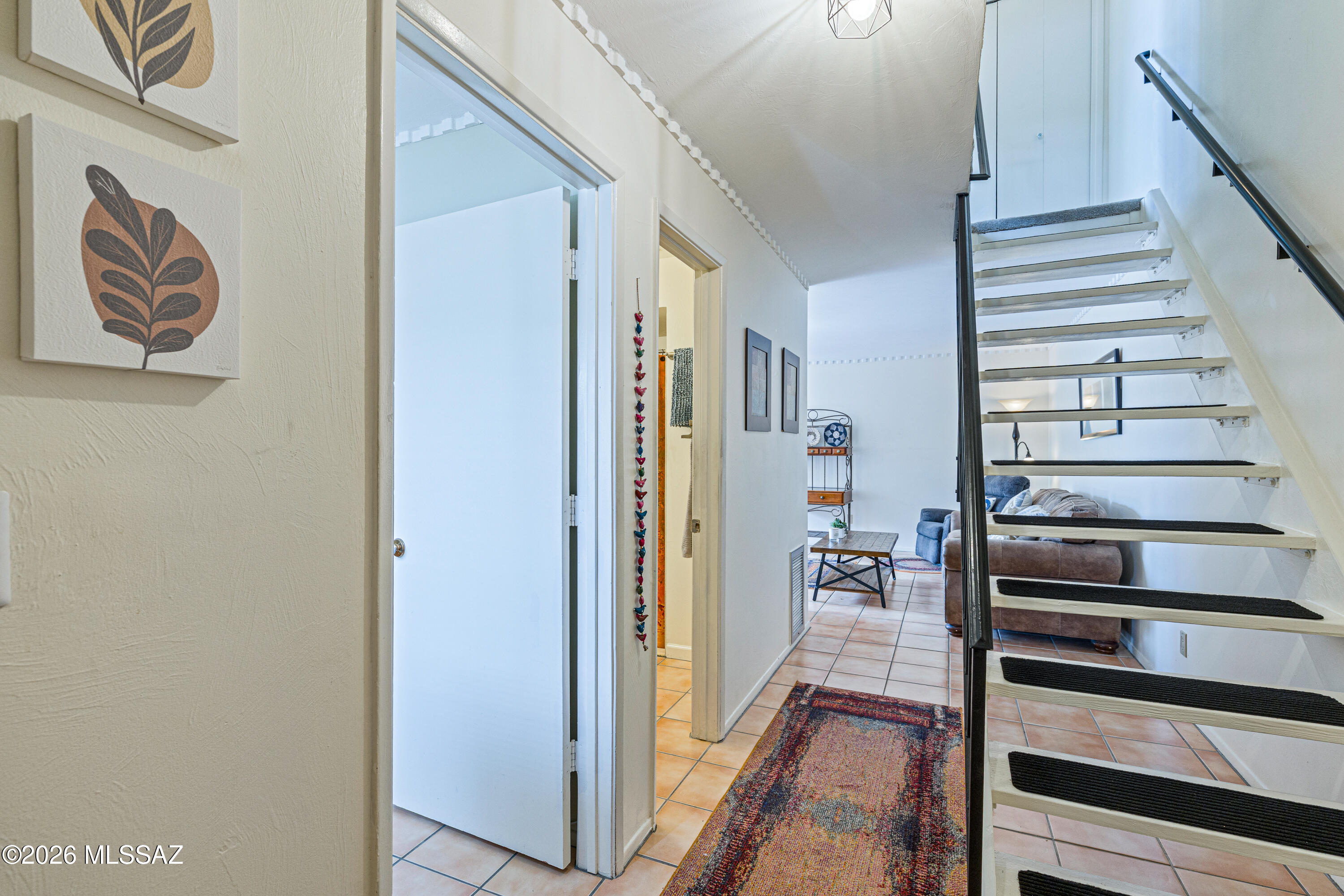 Entry hall with tiled floors and a colorful runner beside an open staircase.
