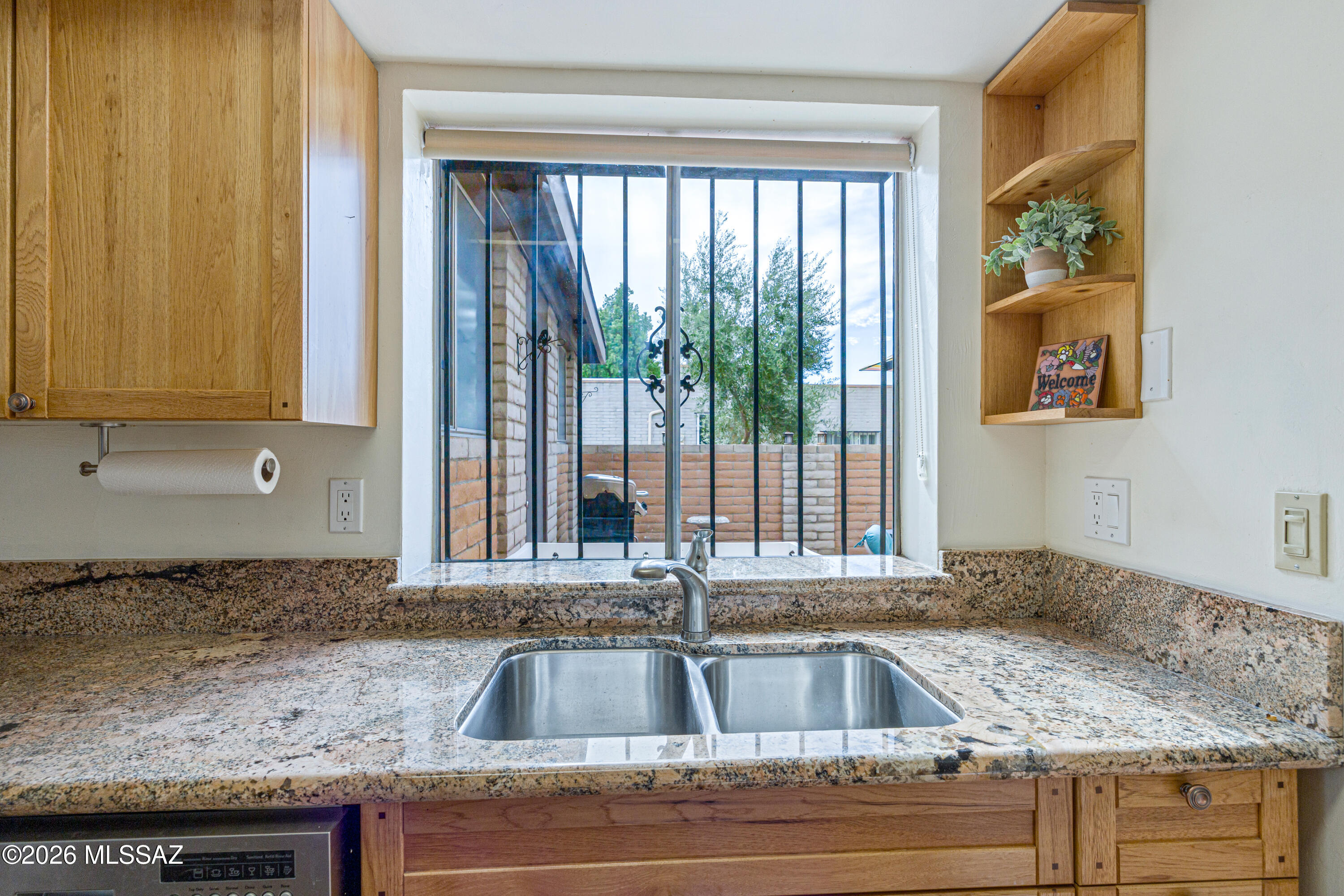 Kitchen sink and granite counters beneath a barred window overlooking a walled courtyard.