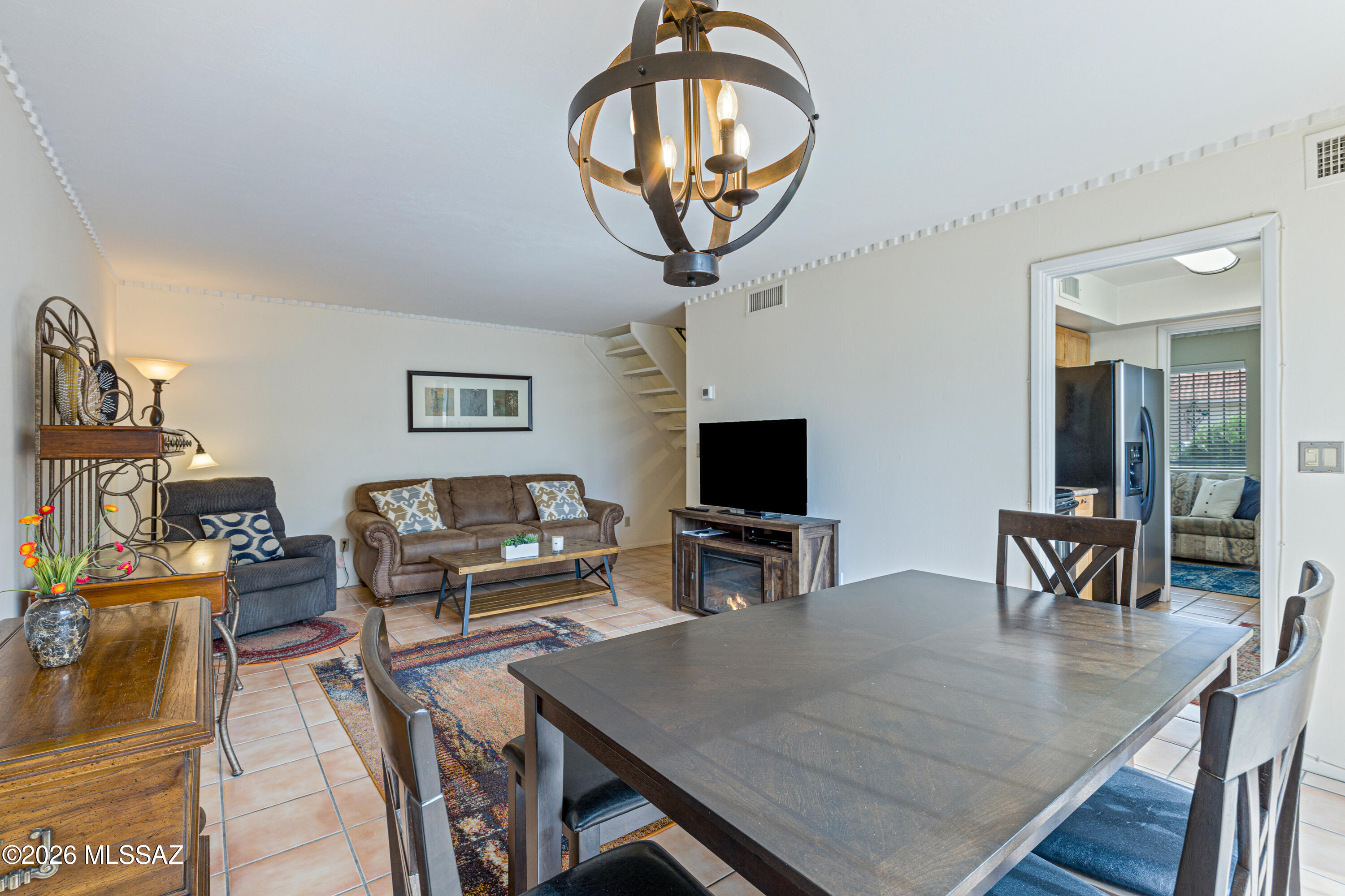 Living and dining area with a large dark dining table, chandelier, sofa, and television beside a fireplace.