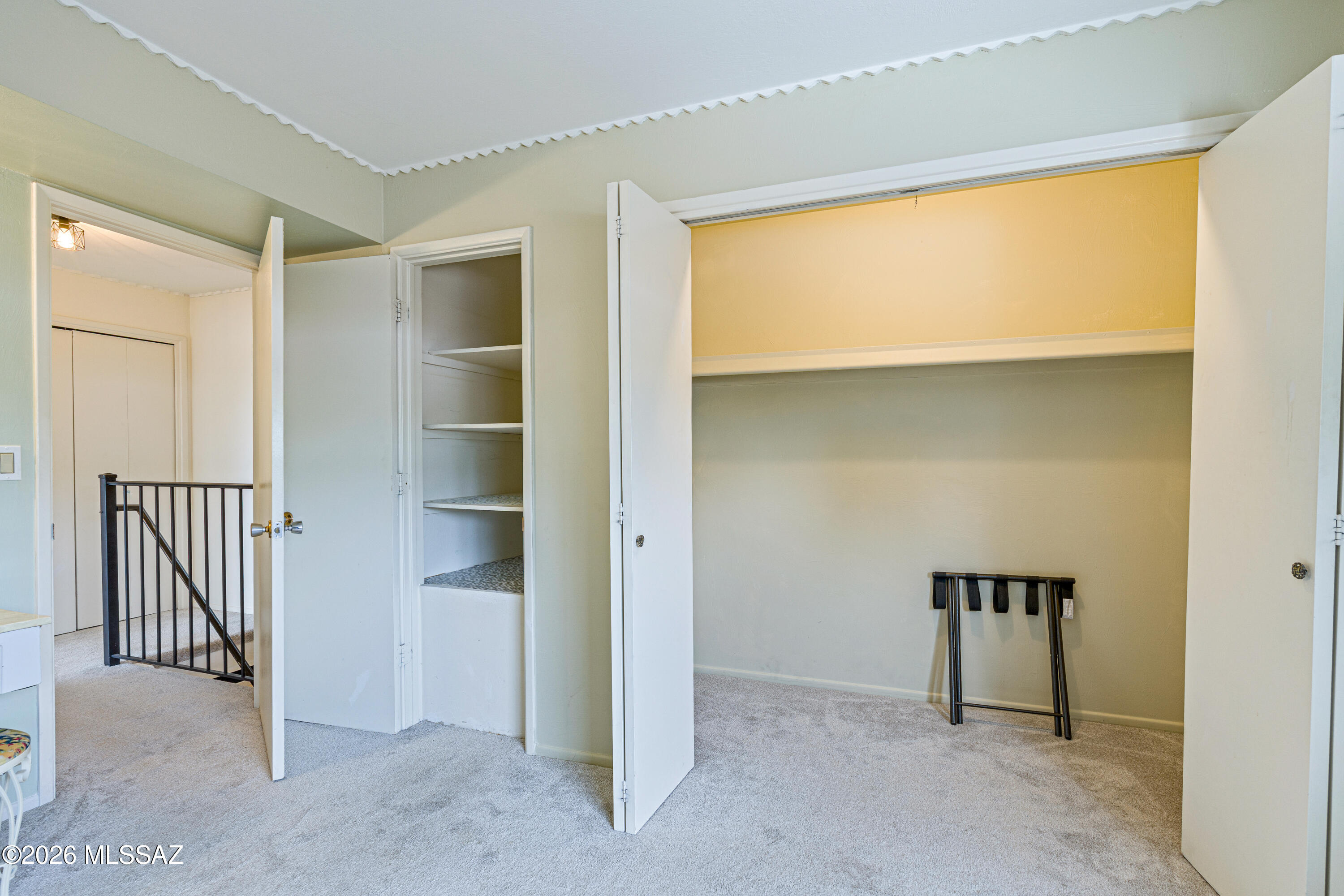 Open bedroom closet with a high shelf and narrow built-in shelving unit.