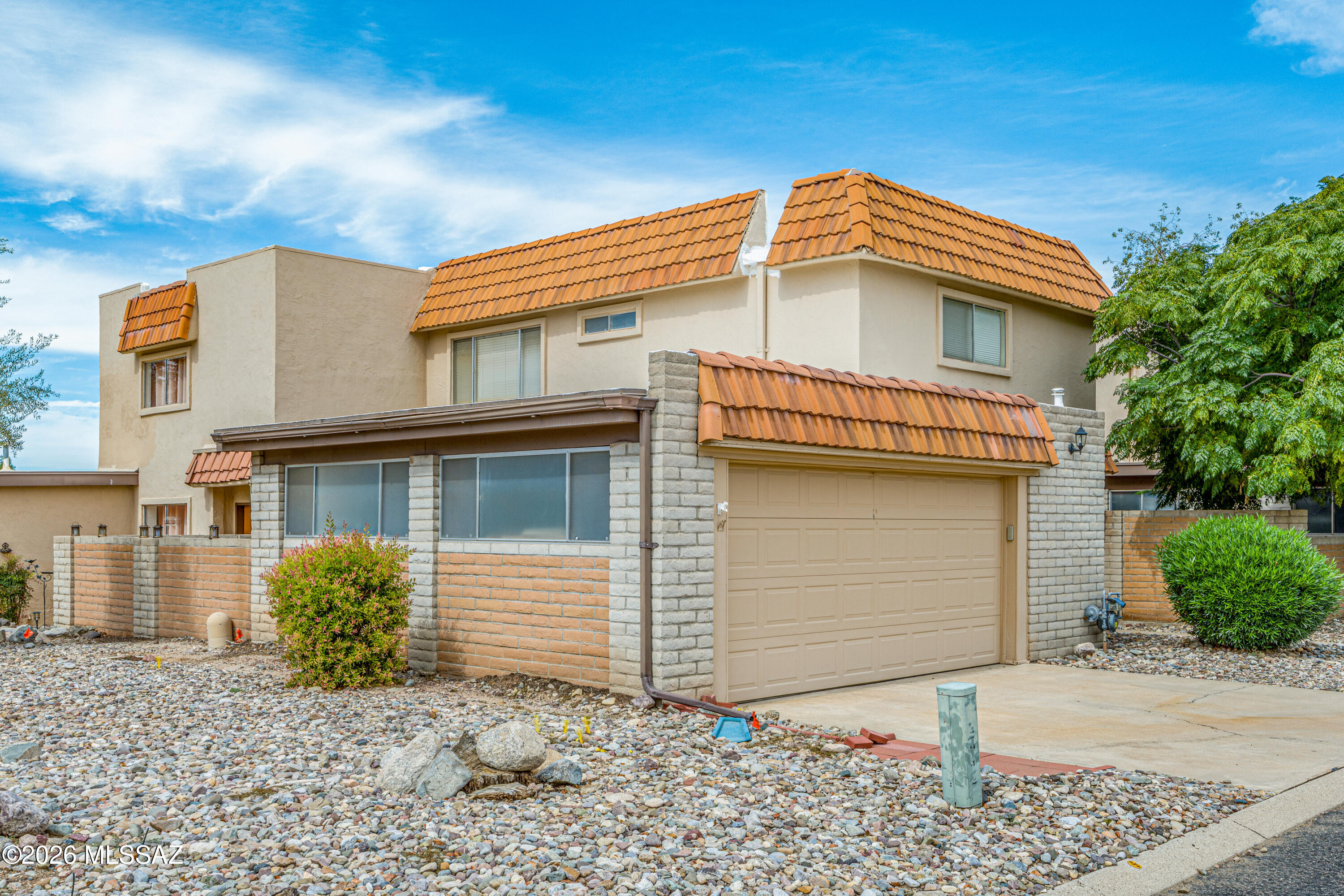 Two-story stucco home with orange tile roofs, a two-car garage, and rock landscaping.