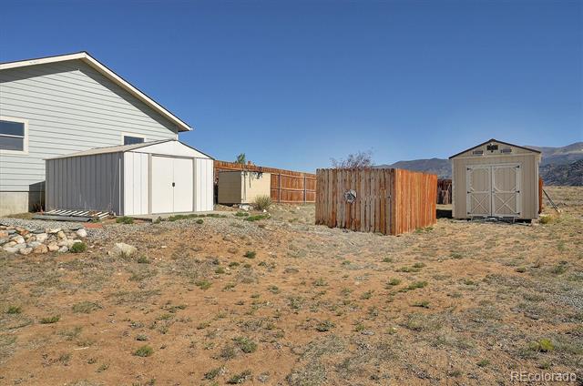 Detached sheds and a fenced storage area beside a house, with mountains in the distance.
