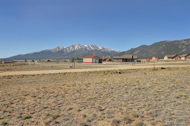 Open rural property beside a road, with scattered buildings and snow-dusted mountains in the distance.
