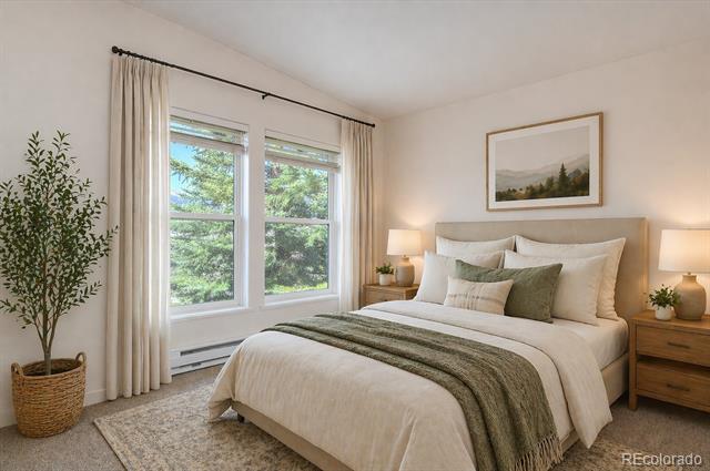 Staged bedroom with a white bed, green throw, matching nightstands, and windows overlooking leafy trees.