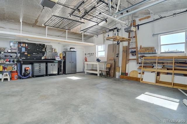 Workshop with concrete floors, tool cabinets, overhead storage racks, and large windows.