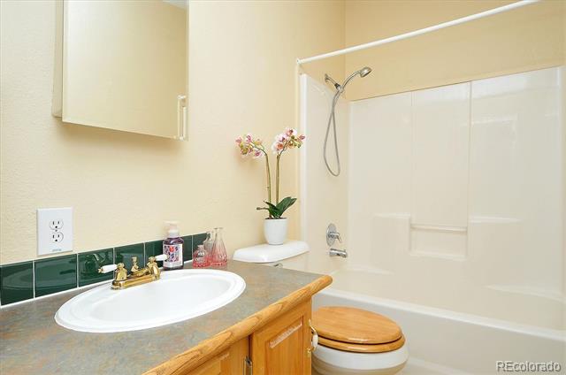 Bathroom with a green-tiled vanity, wooden cabinets, and a bathtub-shower with a white surround.