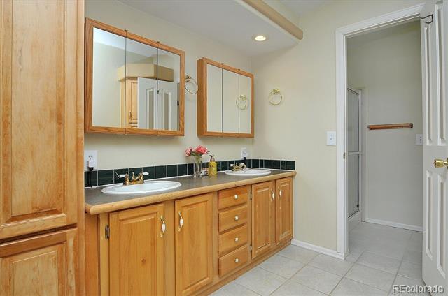 Bathroom with a long wood double vanity, framed mirrors, dark backsplash, and tiled floor.
