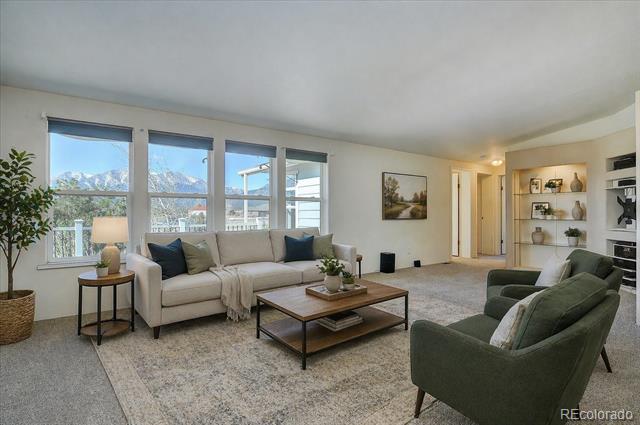 Living room with a light sofa and green armchairs facing windows overlooking snow-covered mountains.