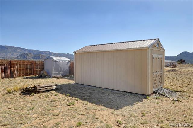 Beige storage shed on a dry rural lot, with mountain ridges in the distance.