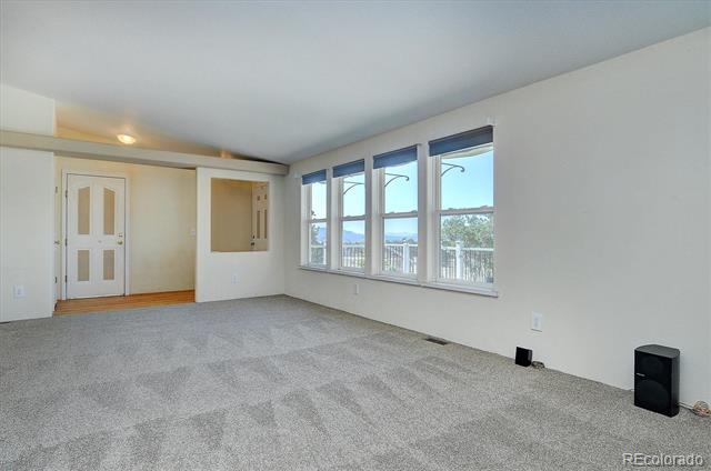Empty carpeted room with a front door and three windows overlooking trees and distant mountains.