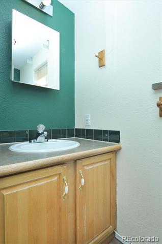 Bathroom vanity with a white oval sink, light wood cabinets, and a large mirror on a teal wall.