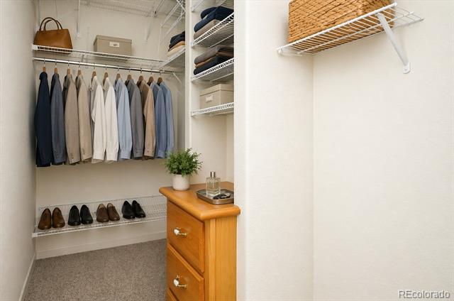 Walk-in closet with hanging clothes, shoes on a shelf, and a wooden chest with a potted plant.