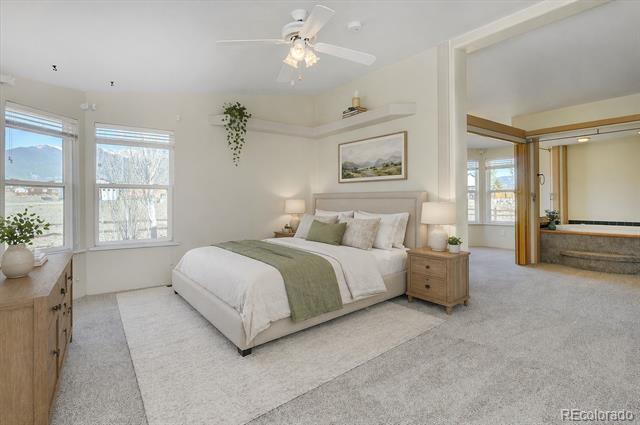 Furnished bedroom with a white bed, green throw, mountain-view windows, and an adjoining bathroom.