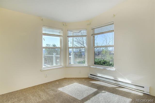 Vacant carpeted room with three tall windows, white blinds, and a long baseboard heater.