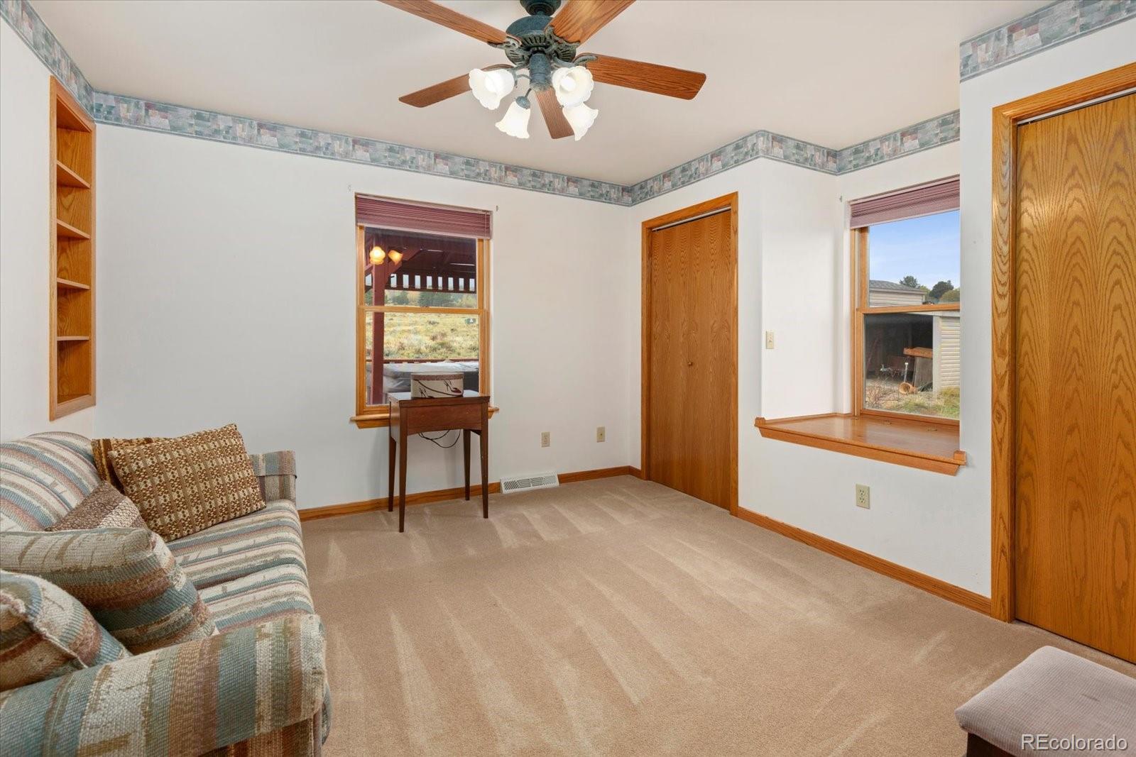 Furnished carpeted room with a patterned sofa, wooden trim, and windows overlooking the yard.