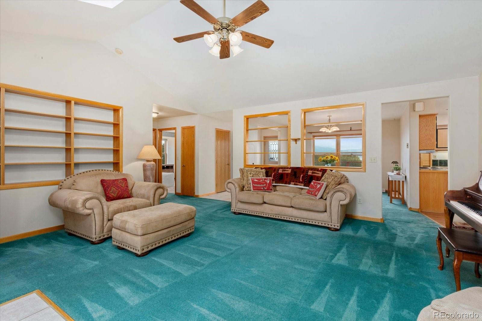 Living room with teal carpet, beige sofas, built-in shelving, and mountain views through the windows.
