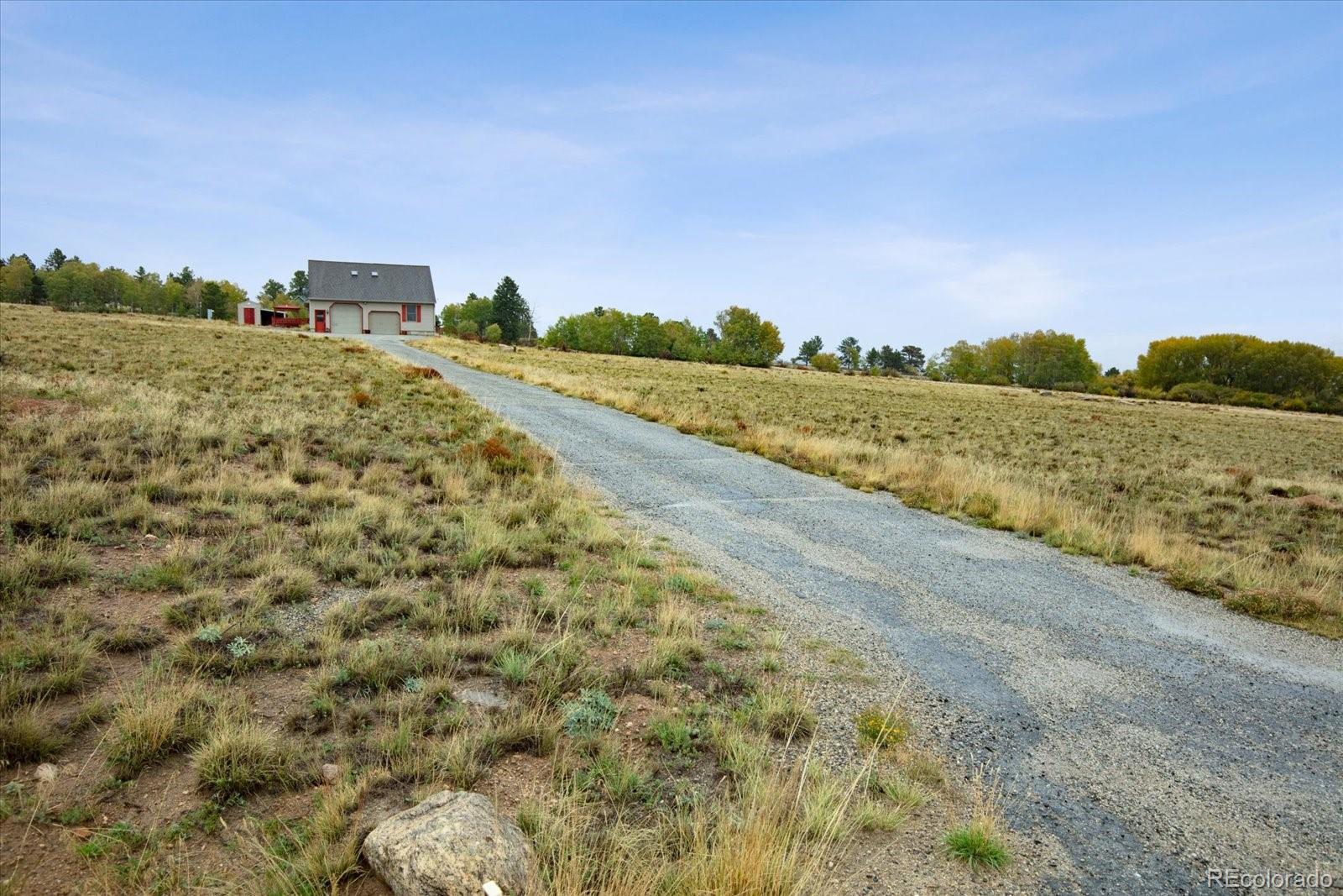 Small red-trimmed garage at the end of a gravel driveway across open grassland.