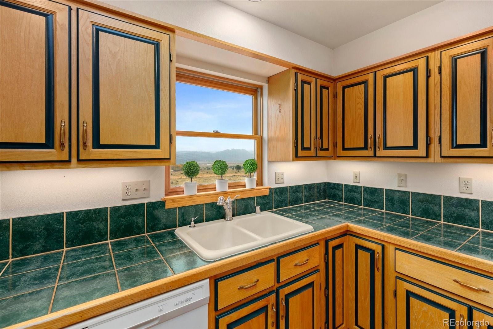 Kitchen with green tile counters, wood cabinets, and a window overlooking a valley and mountains.