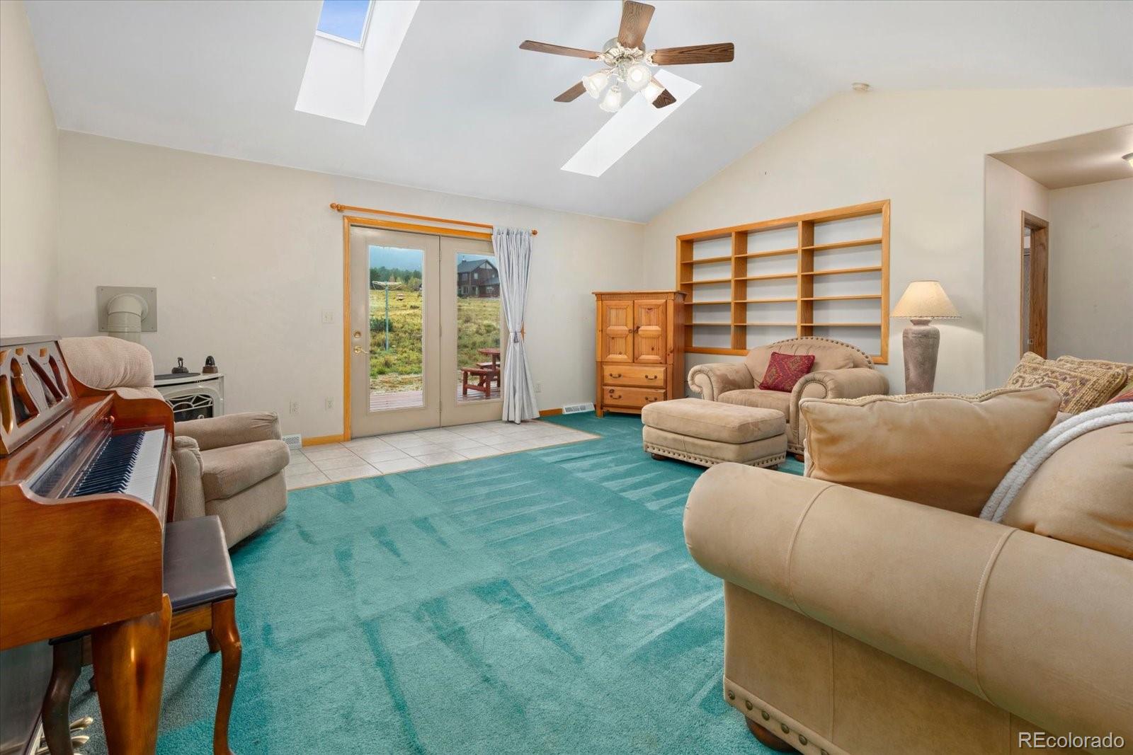 Living room with turquoise carpet, a piano, skylights, and sliding glass doors to a patio.