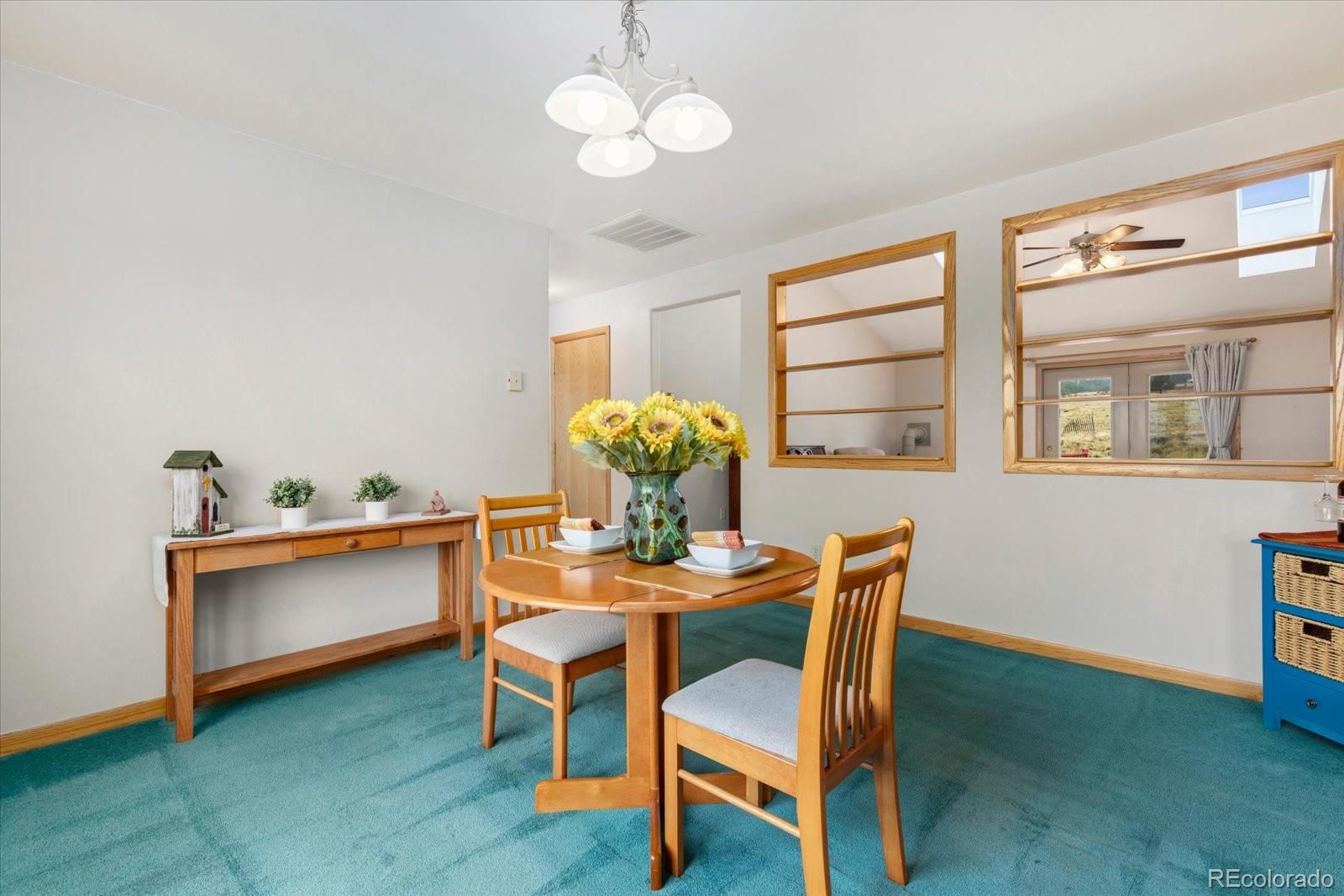 Dining room with a round wooden table, sunflower centerpiece, and turquoise carpet.