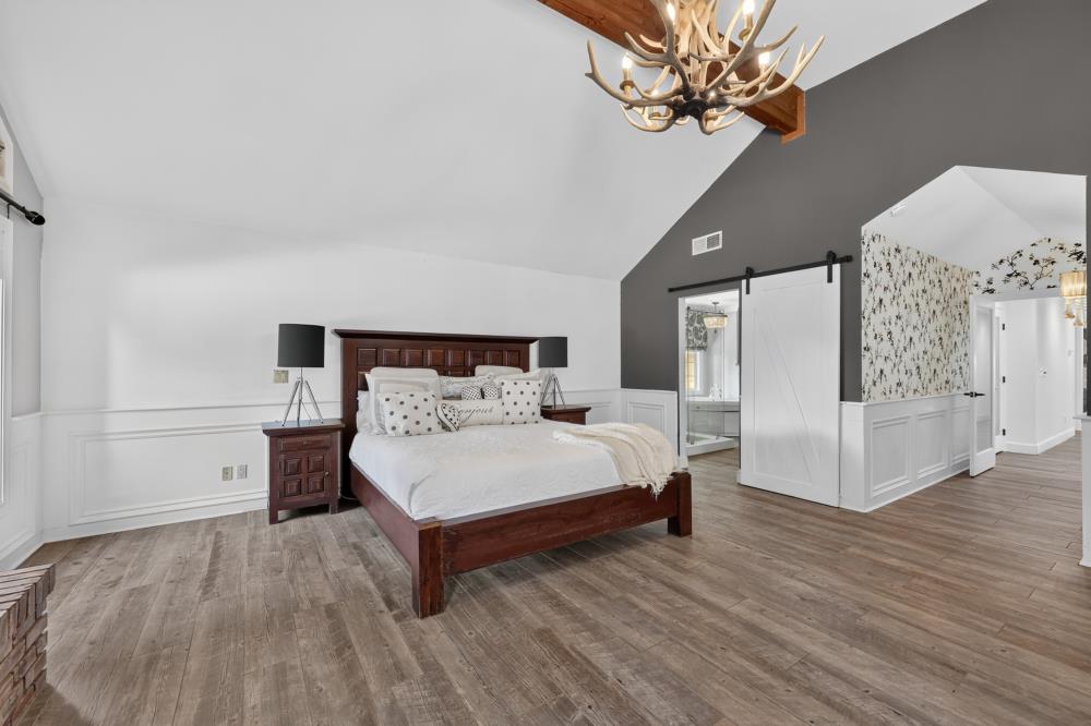 Bedroom with a dark wood bed, vaulted ceiling, antler chandelier, and sliding barn door.