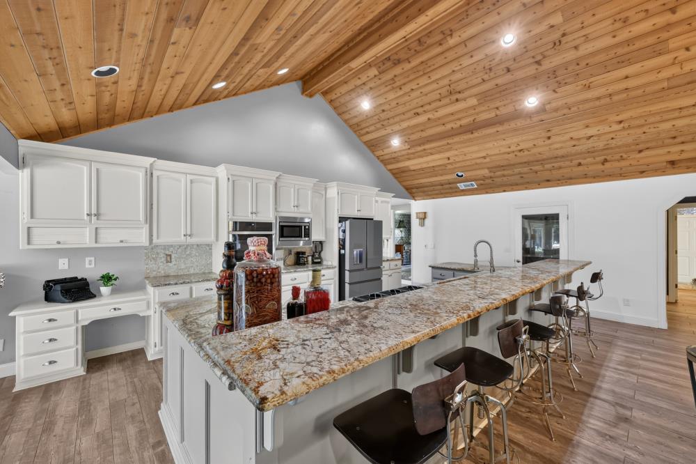 Kitchen with a long granite island, white cabinets, and a vaulted wood-plank ceiling.