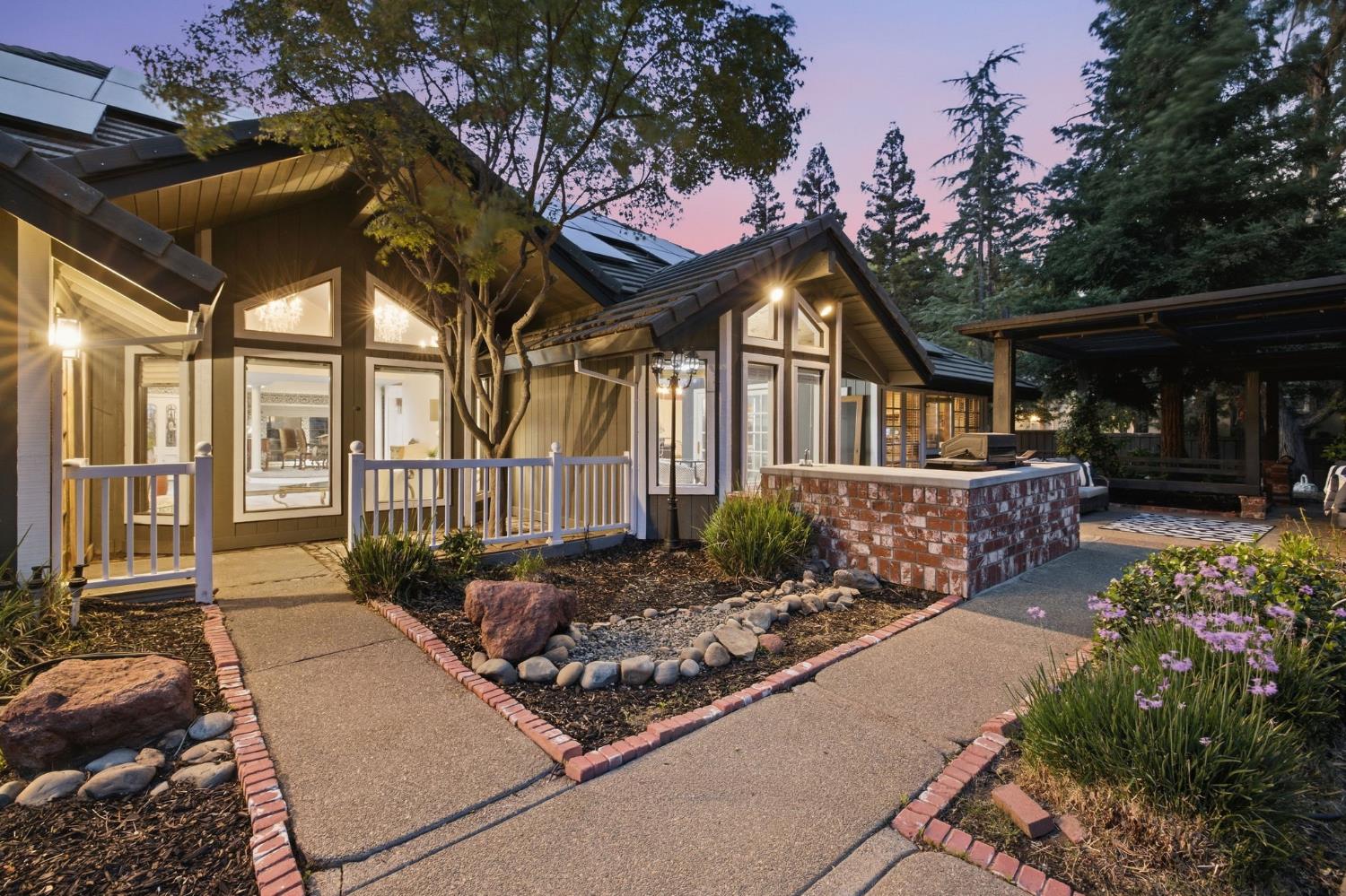 Home exterior at dusk with a covered porch, brick outdoor kitchen counter, and landscaped paths.