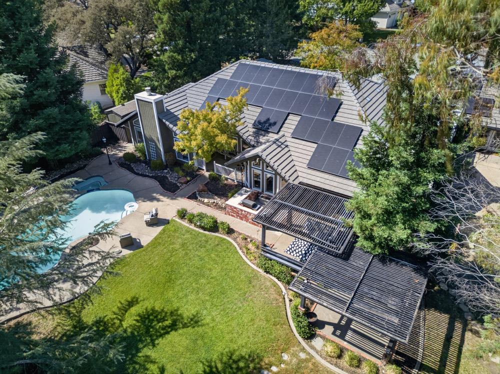 Aerial view of a home with rooftop solar panels, a swimming pool, and a pergola patio.