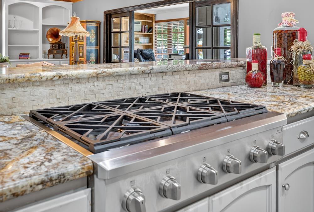 Kitchen with a stainless steel gas range, mottled stone counters, and a raised stone backsplash.