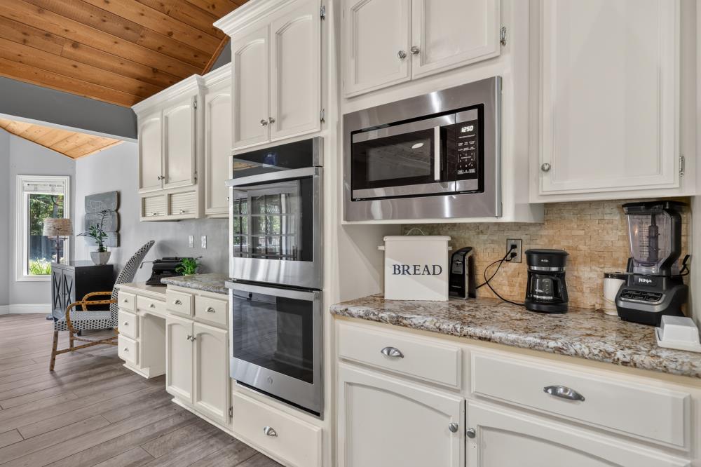 Kitchen with white cabinets, stainless steel double oven, stone counters, and a wood-plank ceiling.