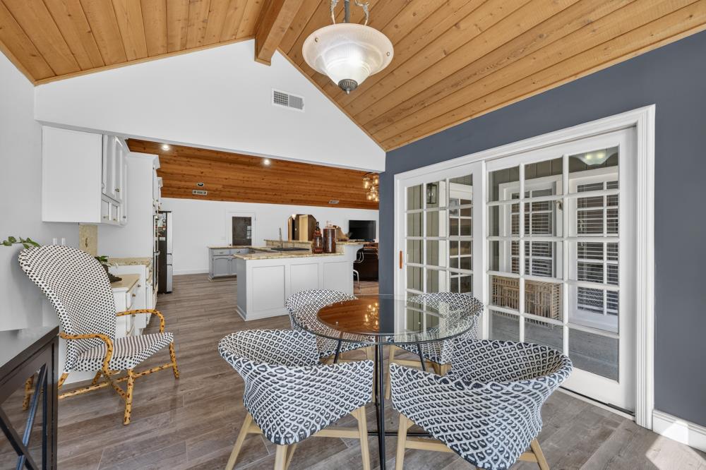 Dining area with patterned chairs around a glass table beneath a vaulted wood ceiling.